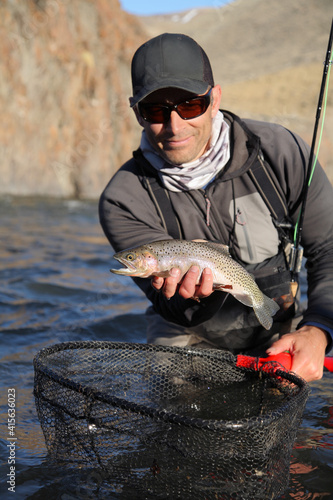 Fotografie happy modern fly fisherman holding fresh-caught cutthroat trout