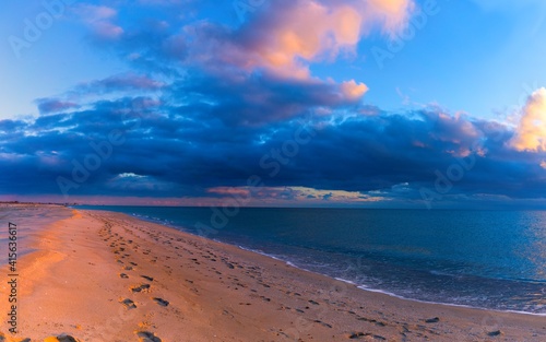 Fototapeta Naklejka Na Ścianę i Meble -  Human footprints on the seashore go into the distance to the horizon. Dramatic evening blue cloudy sky (Seascape)