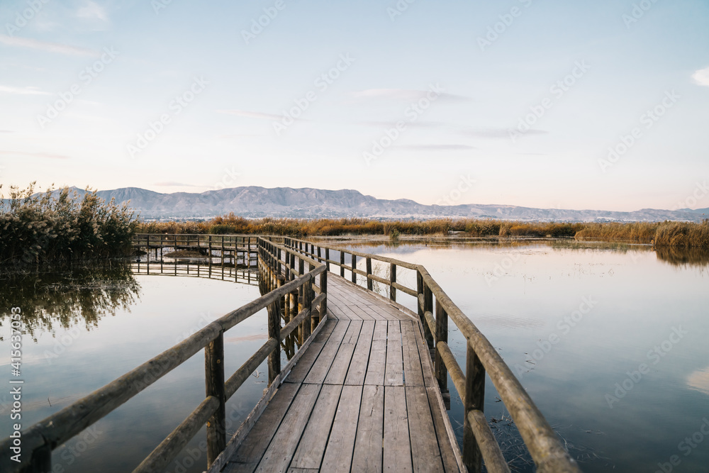 Wooden bridge with calm water on the sides in the natural park called 'El Hondo' in Elche at sunset. Elche, Alicante, Spain