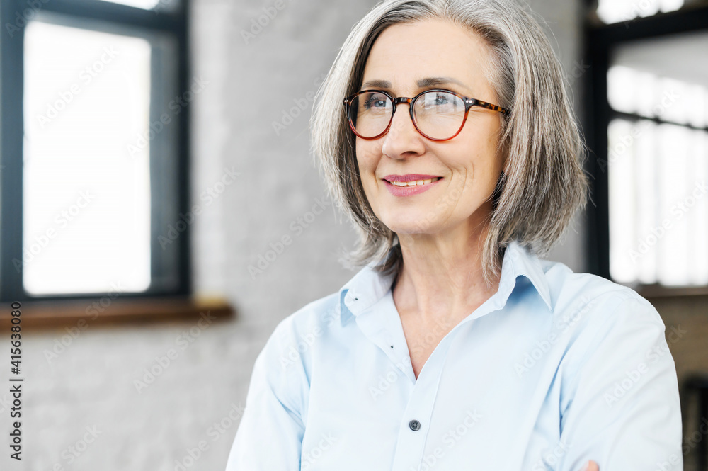 Headshot portrait of a charming smiling elegant senior woman in glasses standing and looking away, thinking of the bright company future. Close-up of a middle-aged gray-haired female business owner Headshot portrait of a charming smiling elegant senior woman in glasses standing and looking away, thinking of the bright company future. Close-up of a middle-aged gray-haired female business owner