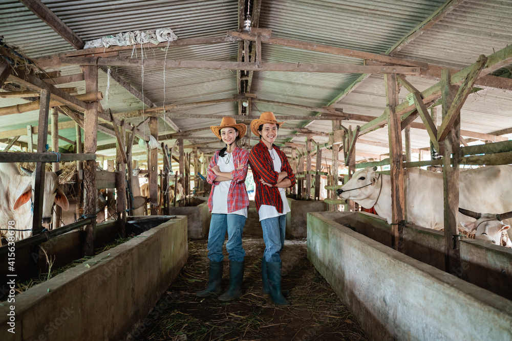 Two cattle breeders wearing casual clothes and hats stand back to back and pose crossed hands in the cattle breeding pen Two cattle breeders wearing casual clothes and hats stand back to back and pose crossed hands in the cattle breeding pen