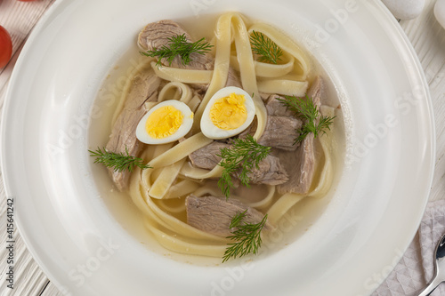 Broth with veal, eggs, noodles on a white wooden table
 photo