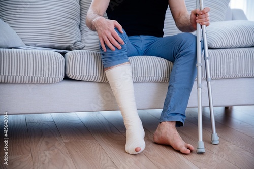 Obraz na płótnie Man with broken leg at home. Leg in plaster. He holds the crutches in his hand. w salonie