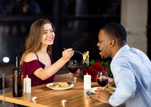 Cheerful interracial couple having fun at dinner in restaurant  woman feeding boyfriend