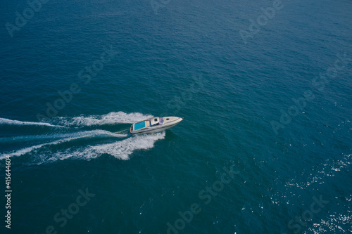 Aerial view luxury motor boat. Drone view of a yacht sailing across the blue clear waters. Top view of a white yacht sailing in the blue sea. © Berg