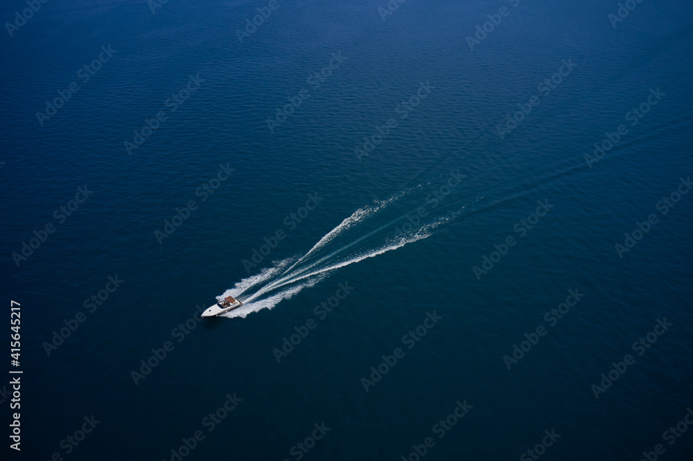 Fototapeta premium The yacht is moving fast on blue water. Top view of the boat. Aerial view luxury motor boat. Top view of a white boat sailing in the blue sea.