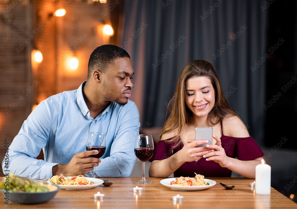 Fototapeta premium Jealous black guy peeking into girlfriend's smartphone, reading her messages