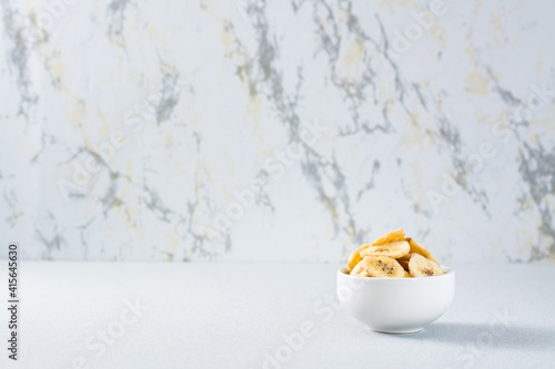 Banana chips in a white bowl on the table. Fast food. Copy space