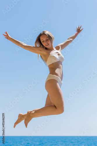 Girl in white swimsuit jumping against sea