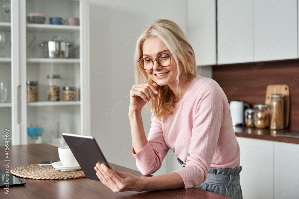 Happy middle aged 50 years old woman using digital tablet sitting