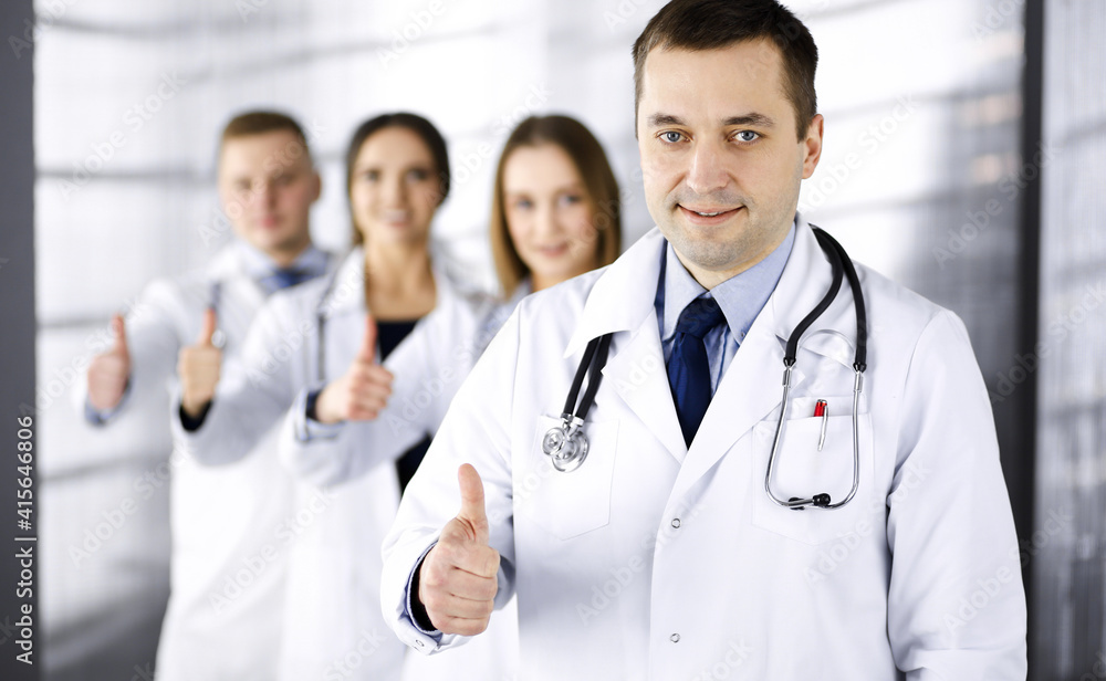 Group of professional doctors are standing as a team with thumbs up in a hospital office, ready to help their patients. Medical help, insurance in health care and medicine concept Group of professional doctors are standing as a team with thumbs up in a hospital office, ready to help their patients. Medical help, insurance in health care and medicine concept