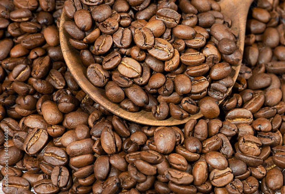 Naklejka premium Grains of coffee in a wooden spoon on a wooden background.