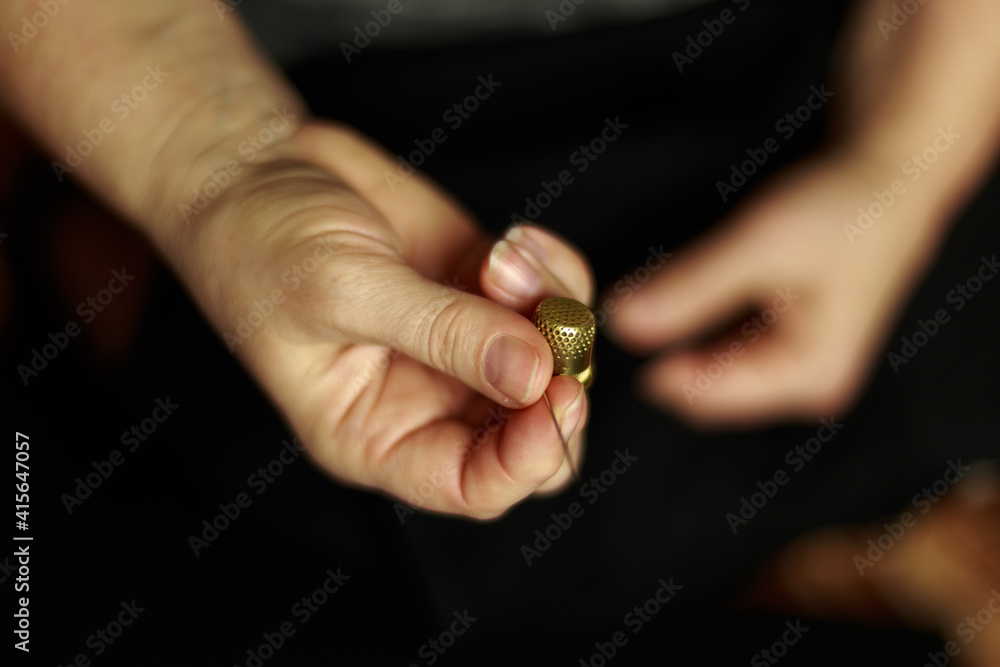 Seamstress's hands. Female hands with a needle, thread and thimble. Woman sews dark clothes. Seamstress's hands. Female hands with a needle, thread and thimble. Woman sews dark clothes.