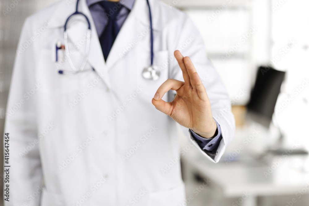 Unknown male doctor standing straight with OK sign in clinic near his working place, closeup. Perfect medical service in hospital. Medicine and healthcare concept Unknown male doctor standing straight with OK sign in clinic near his working place, closeup. Perfect medical service in hospital. Medicine and healthcare concept