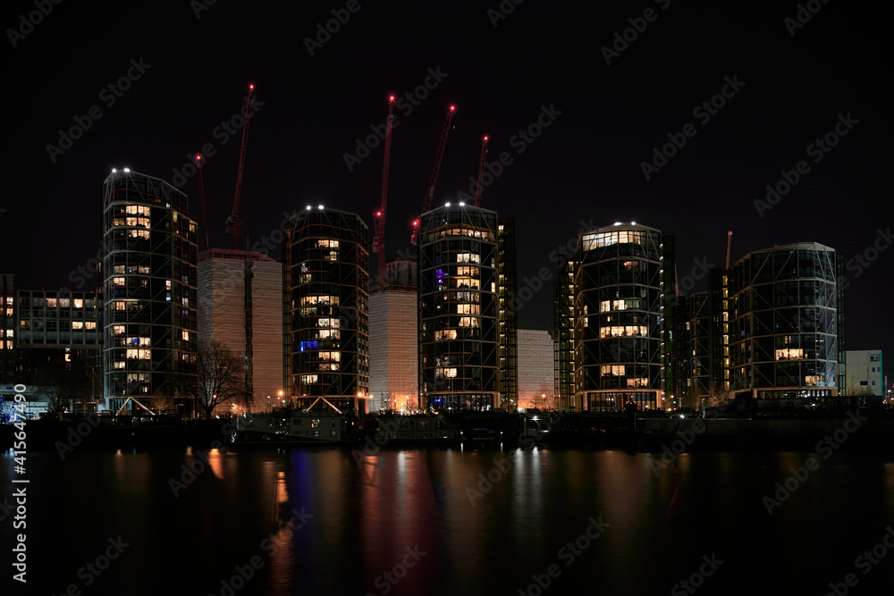 Nighttime view over River Thames to residential apartments and new building construction and cranes with red lights
