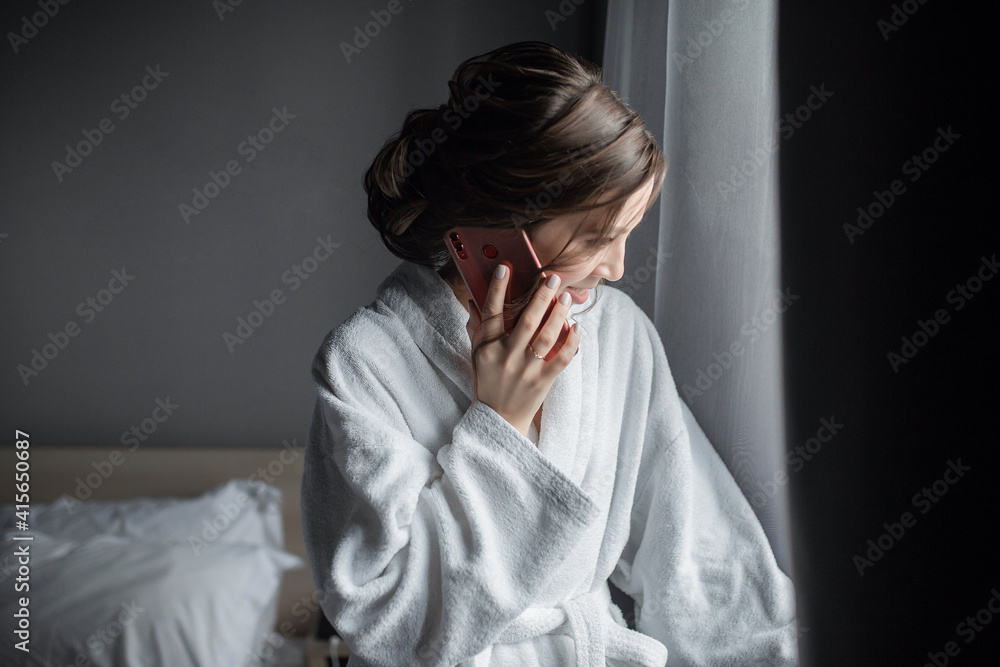 A beautiful young woman is talking in a hotel room in a white lab coat on the phone. Remote work A beautiful young woman is talking in a hotel room in a white lab coat on the phone. Remote work