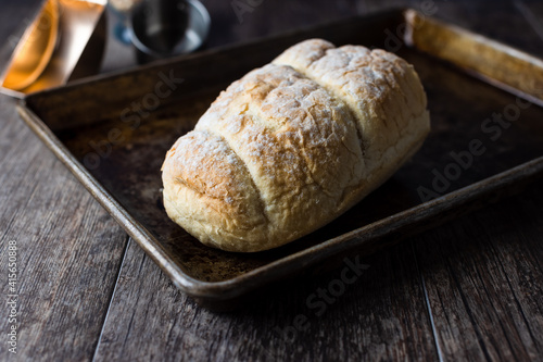 Fresh bread on a baking sheet sitting upon a wooden table top