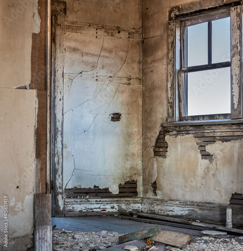 A room in an old, abandoned house with broken plaster, peeling paint and a broken window.  photo
