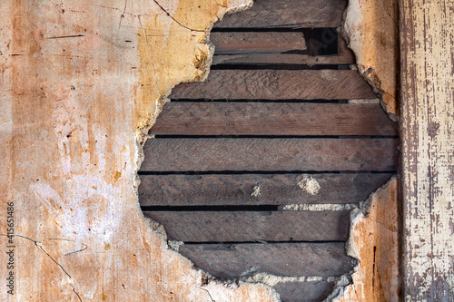 An old wall with damaged plaster, revealing the wooden lath behind the plaster. A hand print is visible on the wall next to the hole.