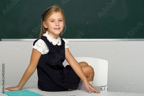 Quadro em tela Adorable schoolgirl sitting on desk in classroom