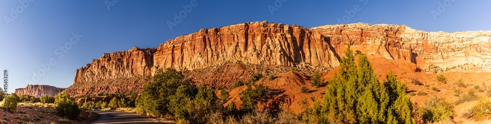 Panorama shot of stripped red sanstone mountain  with green bush and road in capitol reef national park in utah, america