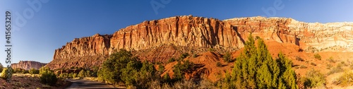 Panorama shot of stripped red sanstone mountain with green bush and road in capitol reef national park in utah, america