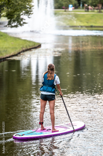 Woman paddling with SUP stand up paddle board in city canal near fountain. Active summer vacations with paddle board. © Uldis Laganovskis