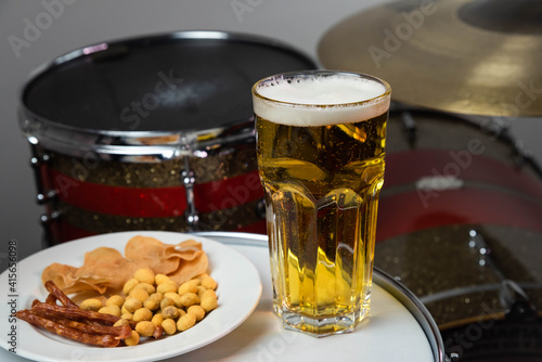 Glass of light beer with salty snacks on professional drum set closeup. Drumsticks, drums and cymbals, at live music rock concert, in the club stage, bar, or in recording studio