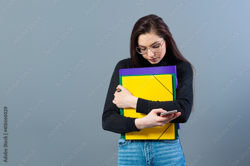 female with smartphone holding a colorfuls folders with documents, isolated on dark background female with smartphone holding a colorfuls folders with documents, isolated on dark background
