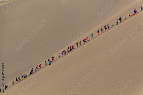 DUNHUANG, CHINA - AUGUST 21, 2018: Tourists climb Singing Sands Dune near Dunhuang, Gansu Province, China photo