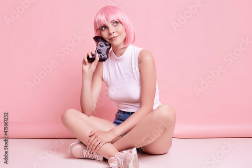 Happy sexy gamer girl with pink hair playing video games using joystick