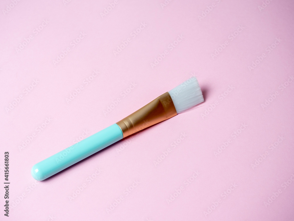 A blue cosmetic brush for applying face masks lies on a pink background. Cosmetic accessories A blue cosmetic brush for applying face masks lies on a pink background. Cosmetic accessories