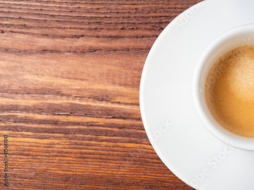 half a cup of freshly brewed Italian espresso coffee on a wooden background. Delicious foam, white cup and saucer. Copy space, a place for the text. An invigorating drink to wake you up