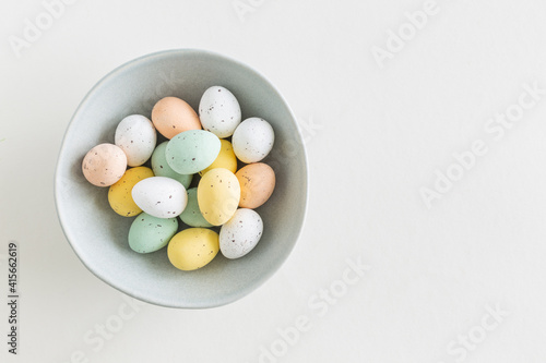 Chocolate easter egg in pastel colors in a blue bowl on a white background, flat lay with copy space