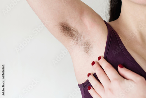 Mujer joven levantando su brazo y mostrando la axila con pelo negro sin afeitar. Concepto bodypositive, feminismo y cuidado corporal. Hermosas axilas femeninas peludas photo