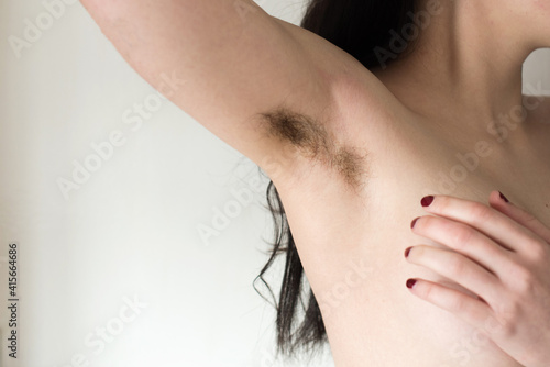 Mujer joven levantando su brazo y mostrando la axila con pelo negro sin afeitar. Concepto bodypositive, feminismo y cuidado corporal. Hermosas axilas femeninas peludas photo