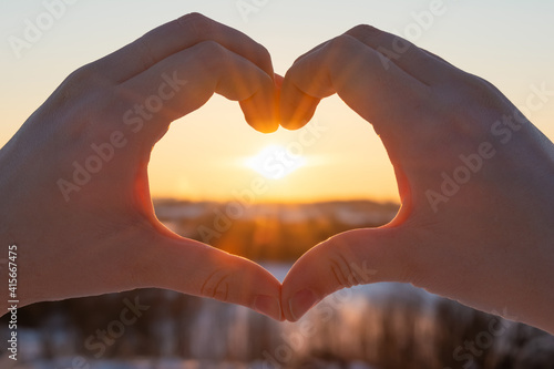 Female hands in the form of heart against the sky pass sunset beams. Hands in shape of love heart