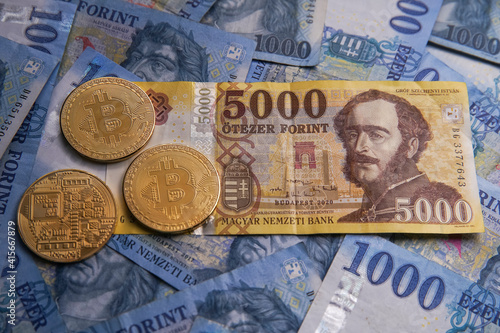 Hungarian banknotes and bitcoin (BTC) digital cryptocurrency coins on a blue background from 1000 HUF paper money.