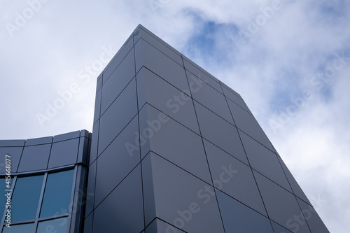 The exterior wall of a contemporary commercial style building with aluminum metal composite panels and glass windows. The futuristic building has engineered diagonal cladding steel frame panels. 