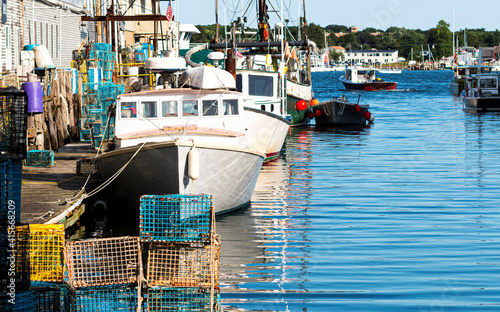 Lobster fishing boats docked in a canal with lobster traps pilled on the dock in Portland Maine