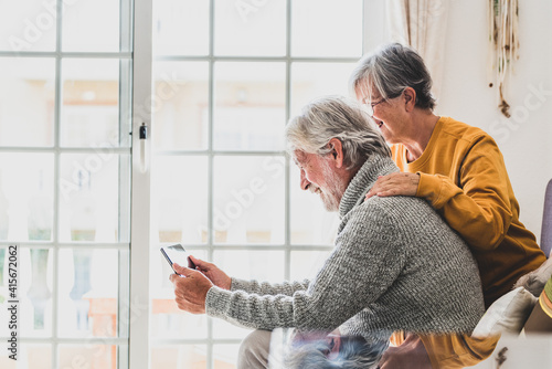 Photography couple of two cheerful and happy mature and old people seniors using tablet and having fun sitting on the sofa at home together