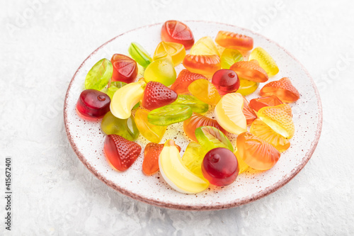 Various fruit candies on plate on gray concrete background. side view.