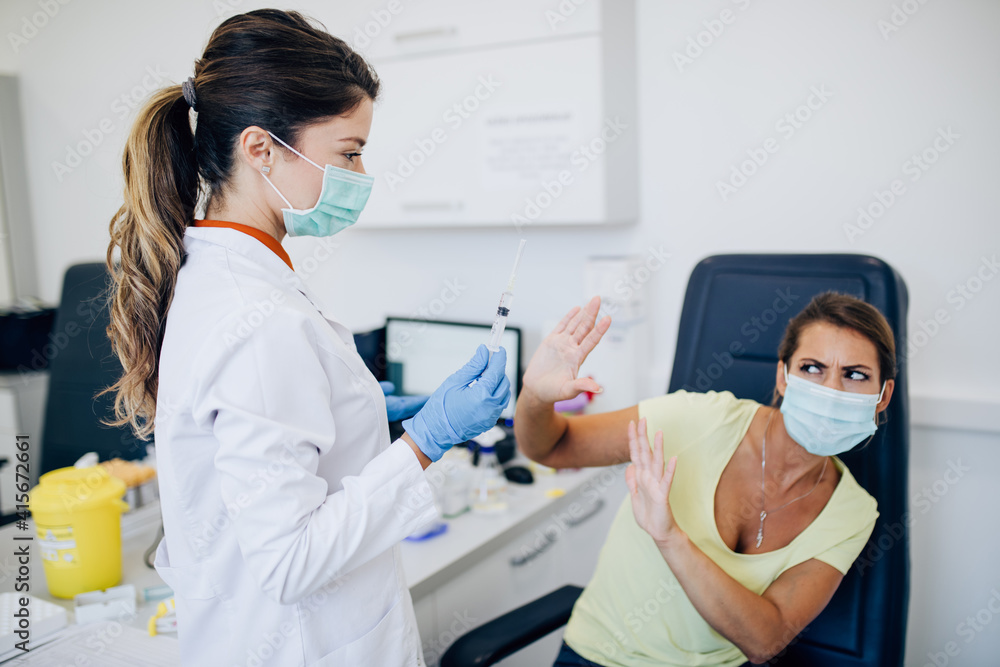 Female doctor or nurse trying to give shot or vaccine against virus to a scared patient. Angry and distrustful patient refuses to receive it. Female doctor or nurse trying to give shot or vaccine against virus to a scared patient. Angry and distrustful patient refuses to receive it.