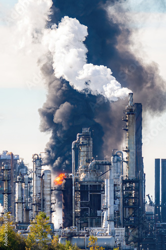 Fire and black smoke at an oil refinery after an explosion. Towers visible in front of smoke and flame. Scene slightly blurred due to volatile air.