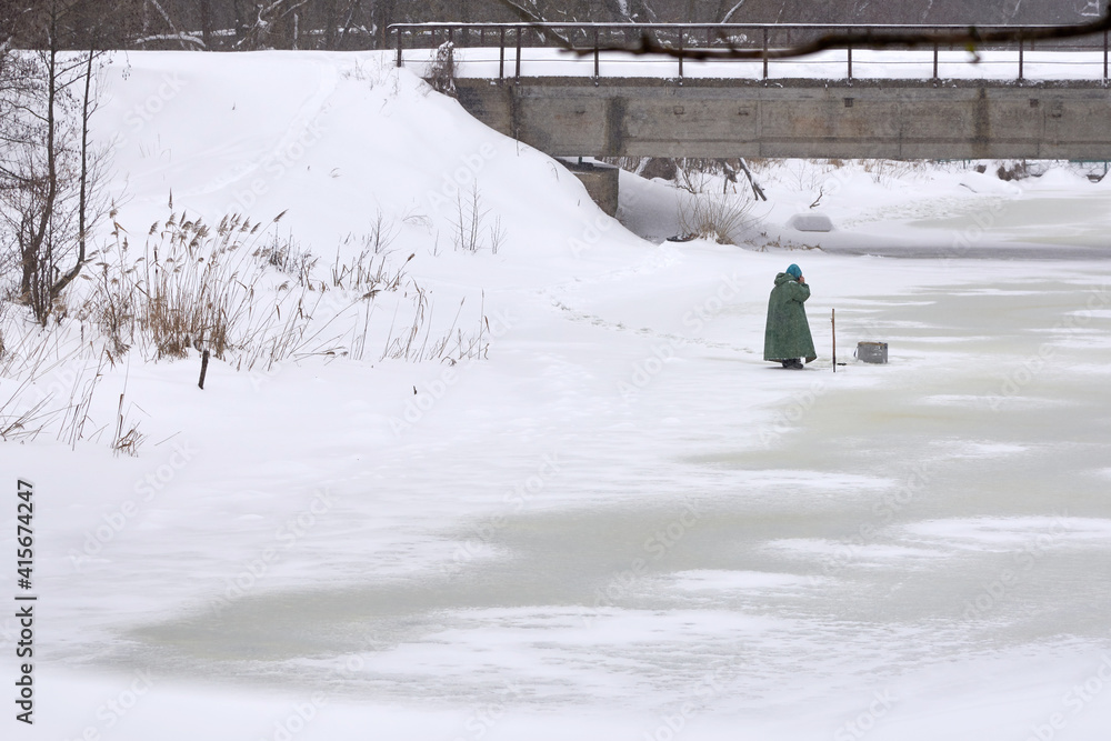 Obraz premium A fisherman speaks on the phone on a frozen river under a bridge.