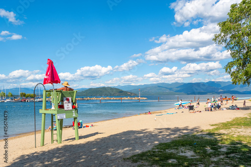 Fototapeta Naklejka Na Ścianę i Meble -  A male lifeguard sits on duty in a lifeguard station at the sandy Sandpoint City Beach along Lake Pend Oreille in the northwest of the USA at summer.