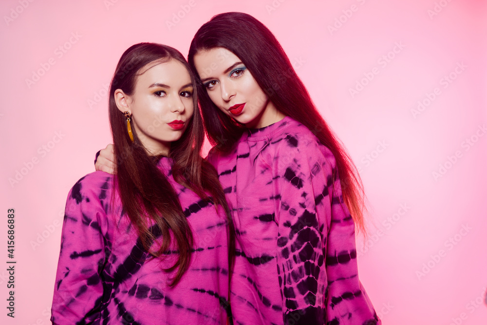 2 girls in the same things with bright makeup. Brunette girls, sisters, girlfriends, twins. Women's power, March 8, Women's Day. Clothing store for teens. Pink color in clothes, pink background. 2 girls in the same things with bright makeup. Brunette girls, sisters, girlfriends, twins. Women's power, March 8, Women's Day. Clothing store for teens. Pink color in clothes, pink background.