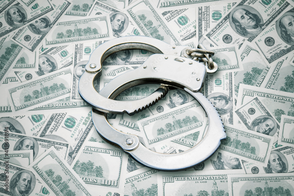 Handcuffs over stack of dollar banknotes Handcuffs over stack of dollar banknotes