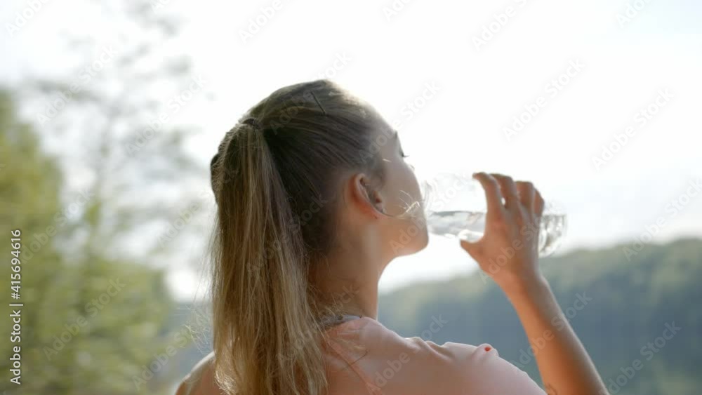 Woman drinking water from bottle in front of lake Woman drinking water from bottle in front of lake