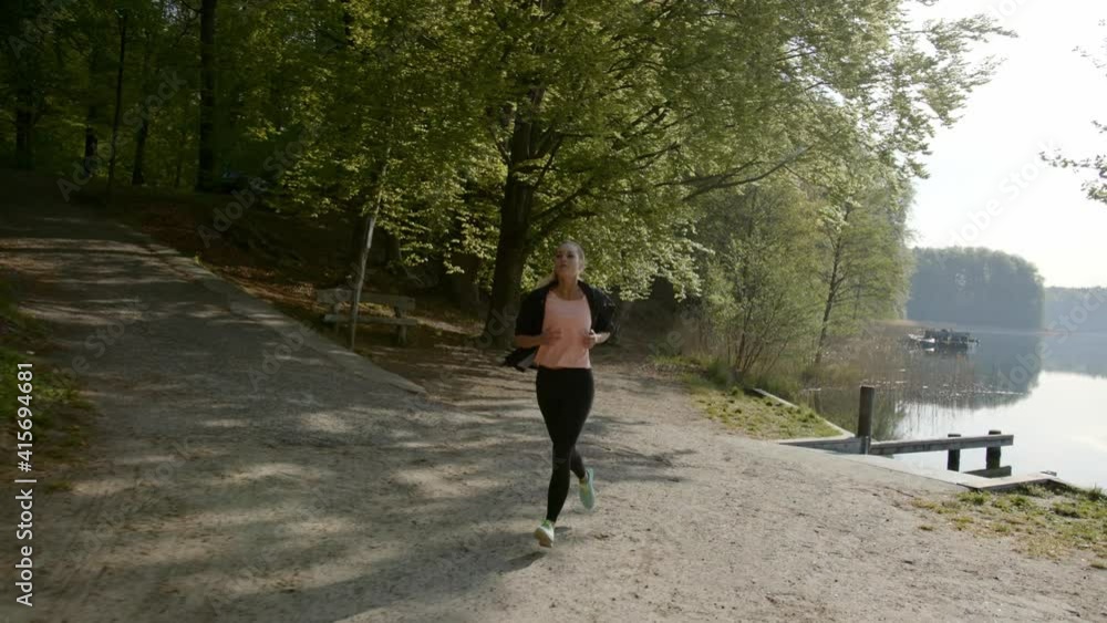 Woman running next to lake and woods on sunny day Woman running next to lake and woods on sunny day